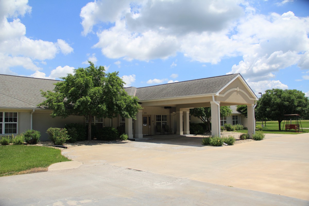 A view of a building entrance with a driveway, surrounded by trees under a partly cloudy sky.