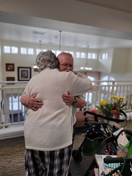 An emotional reunion as two elderly people share a heartfelt hug indoors.