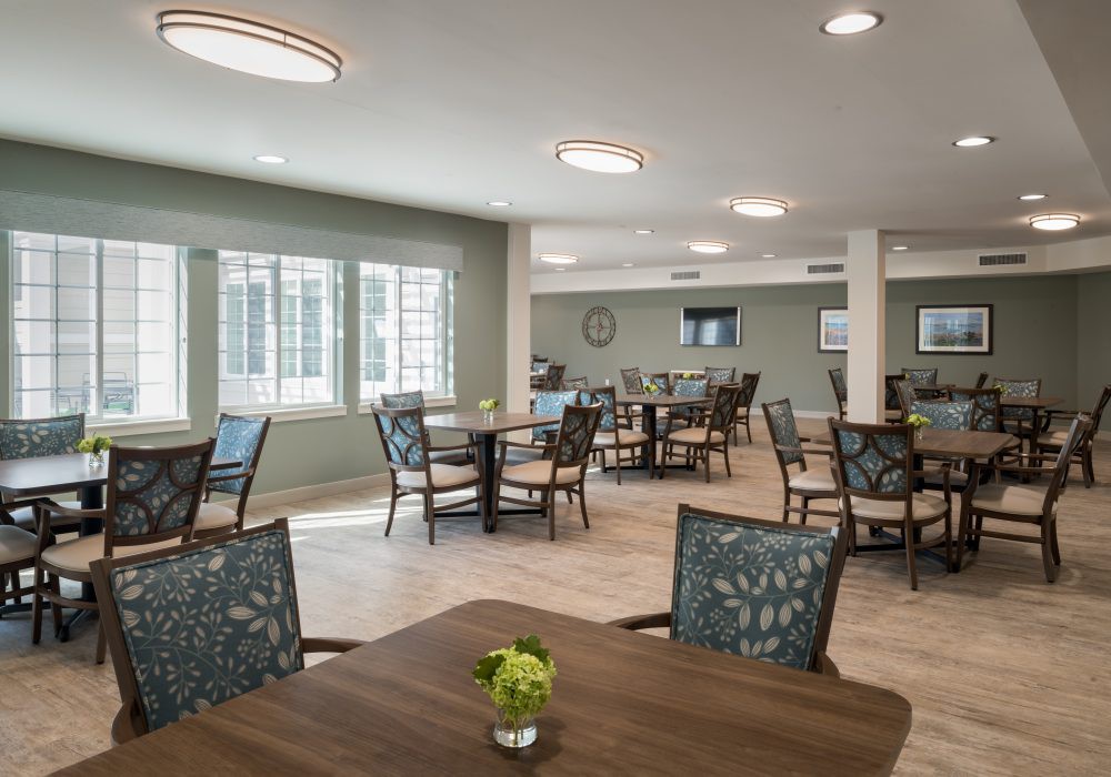 A modern dining area with multiple tables and chairs, featuring ample natural light.
