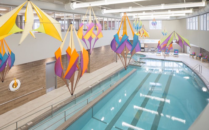 An indoor swimming pool featuring colorful geometric art installations hanging from the ceiling.