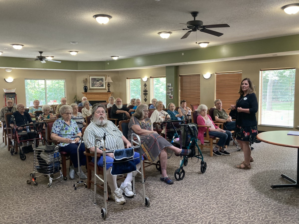 A group of senior citizens gathered indoors for a community event, some using wheelchairs.