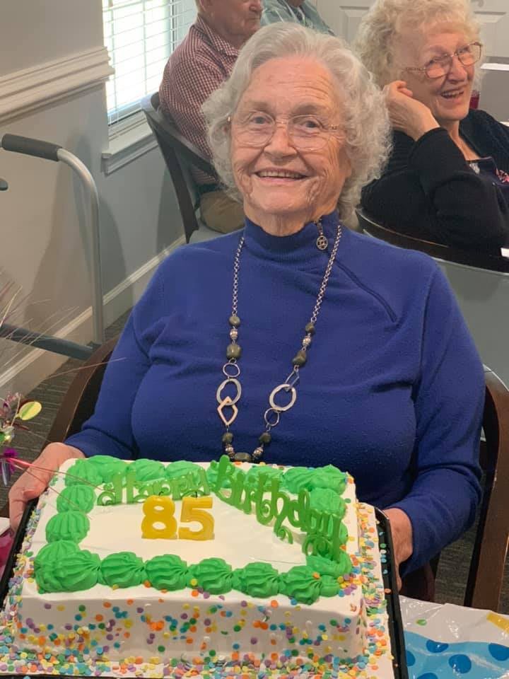 An elderly woman joyfully holding a decorated birthday cake.