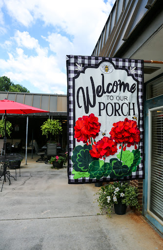 A cheerful 'Welcome to Our Porch' sign adorned with vibrant red flowers, inviting guests to enjoy the outdoor seating area.
