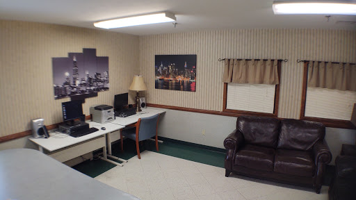 A cozy office space featuring a work desk, computer setup, comfortable chair, and a sofa, complemented by cityscape wall art.