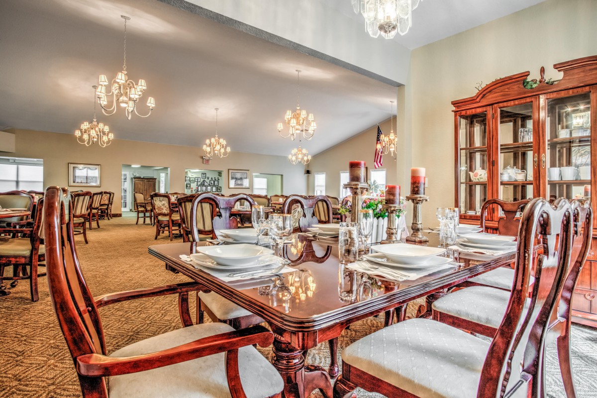An elegant dining room with ornate chandeliers, a polished wooden table set for a meal, and classic furniture.