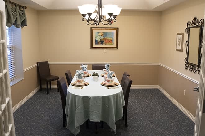 A neatly arranged dining room with a table set for four, illuminated by a chandelier and adorned with wall art.
