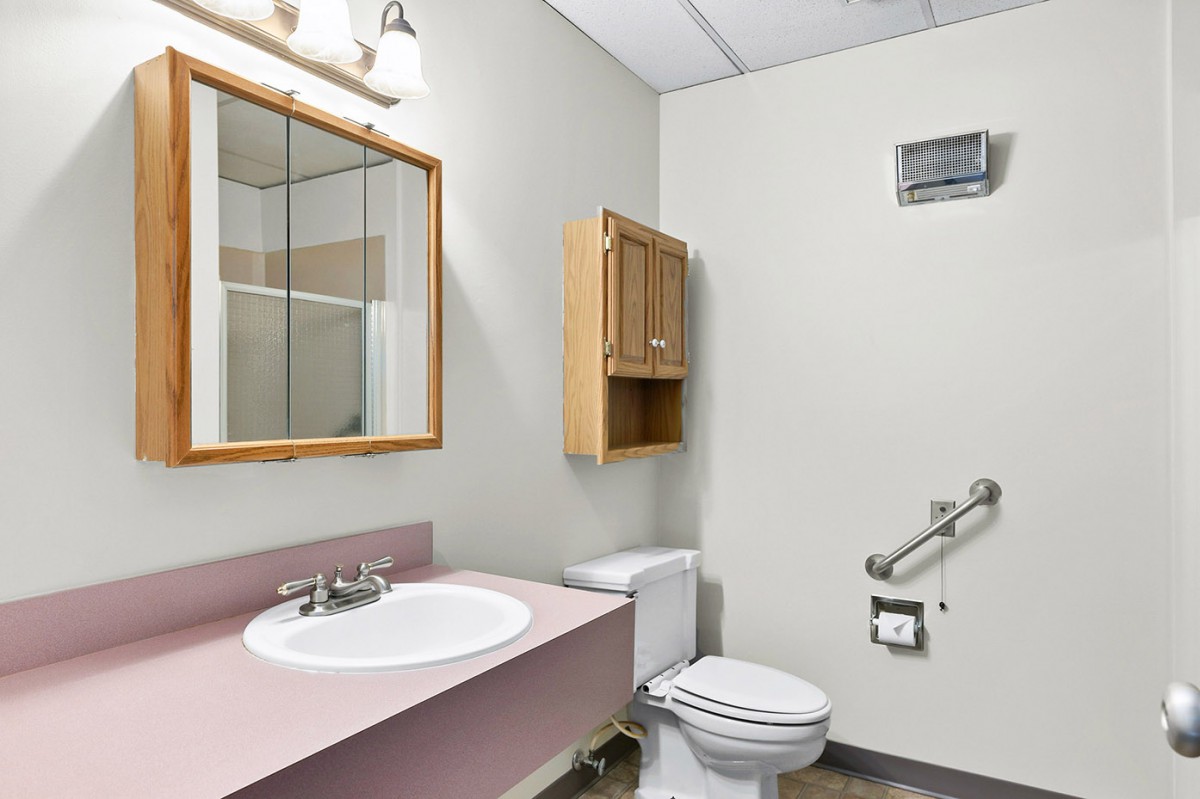 A small bathroom with a sink, toilet, mirror, and wall cabinet.