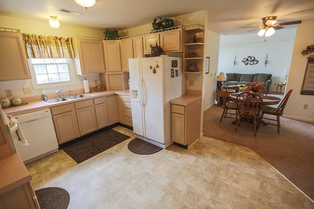 A cozy kitchen with wooden cabinets and a white refrigerator, leading to an adjoining dining area.