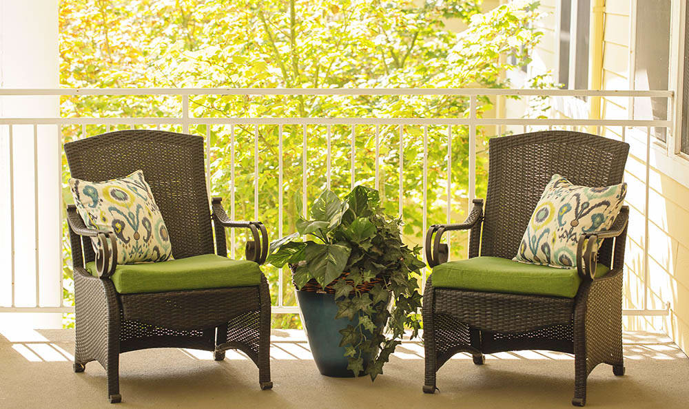 A cozy patio setup with two wicker chairs and a potted plant between them.