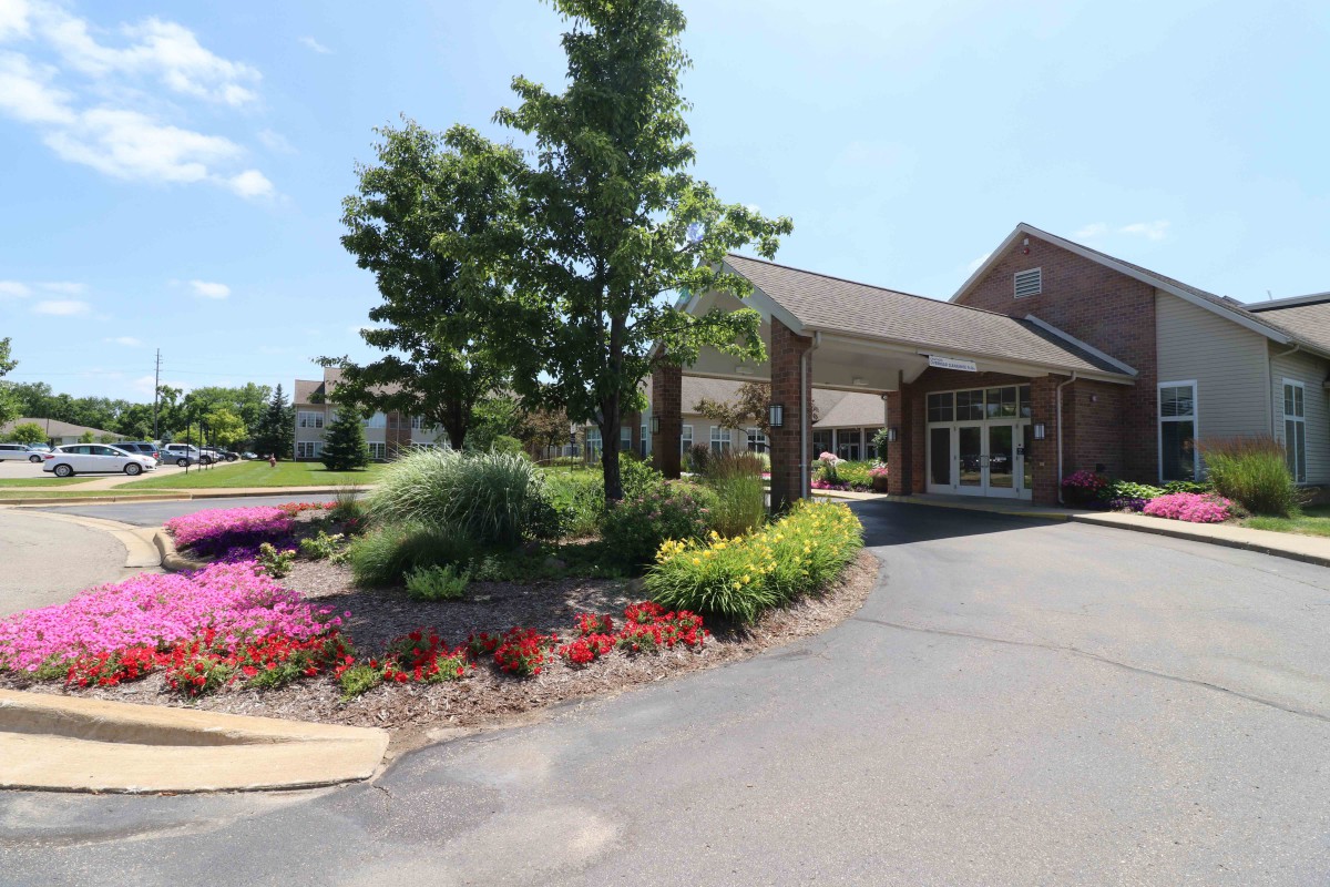 A well-landscaped building entrance with colorful flower beds and a tree on a sunny day.