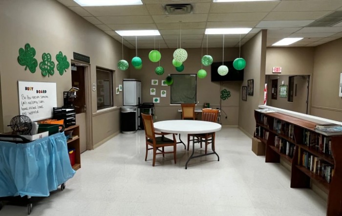 A decorated room with tables, chairs, and green balloons hanging from the ceiling.