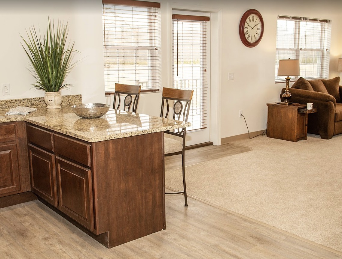 A cozy kitchen interior featuring a wooden counter with chairs, large windows, and stylish decor.