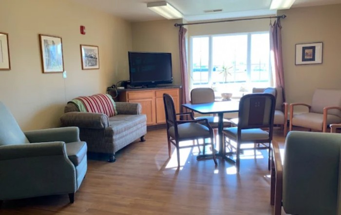 A cozy living room area with a sofa, chairs, table, and a TV near the window.