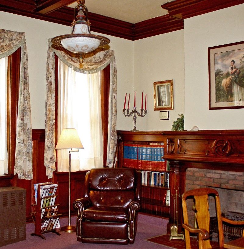 A vintage living room featuring a leather armchair, fireplace, and bookshelves, adorned with wooden accents and classic decor.