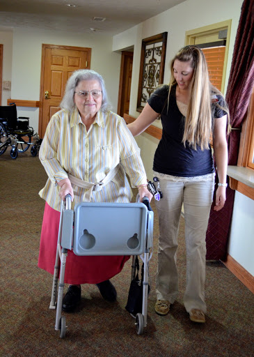 An elderly woman is assisted by a caregiver using a walker in a community setting.
