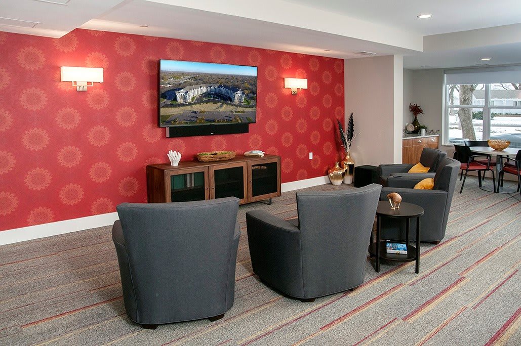 A modern living room with gray chairs, a flat-screen TV, and vibrant red patterned wallpaper.