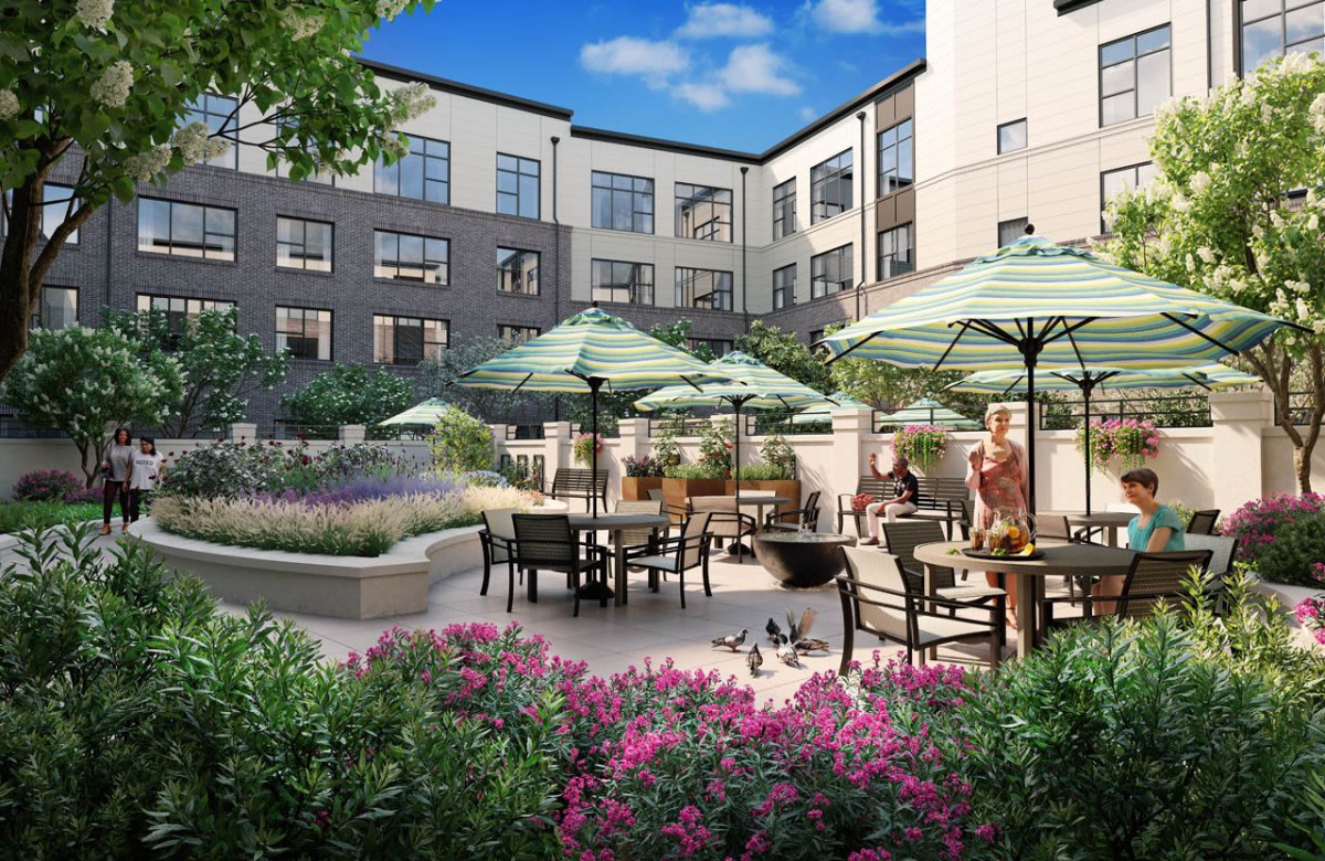 A beautifully landscaped courtyard with patio seating and umbrellas, surrounded by a multi-story building.
