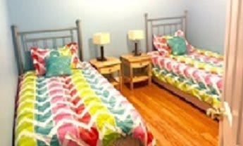 A cozy bedroom with twin beds featuring colorful bedding and matching nightstands with lamps.