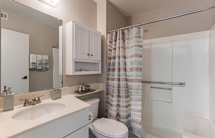 A modern and clean bathroom with a shower curtain, toilet, sink, and wall-mounted cabinet.