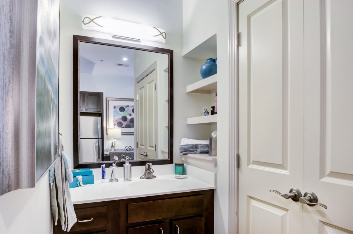 A modern bathroom with a large mirror, sink, and open shelving for storage.