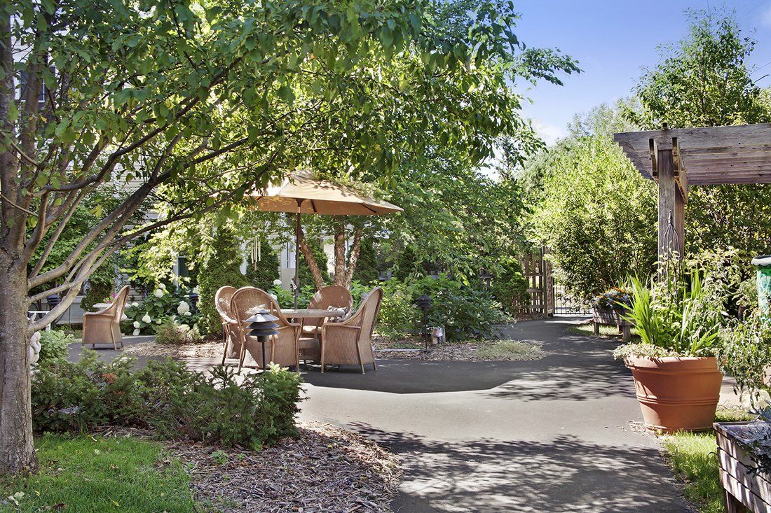 A serene garden patio with a table, chairs, and an umbrella surrounded by lush greenery.
