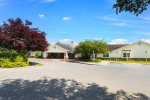 A bright, sunny day at a residential or community building with surrounding trees and a driveway.