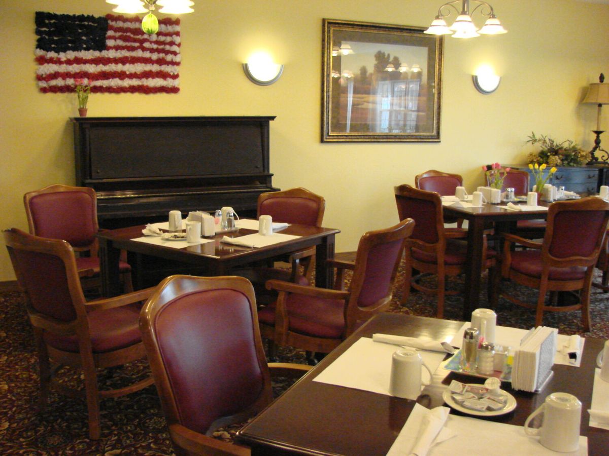 A cozy restaurant dining area featuring tables set with place settings, a piano, and an American flag on the wall.