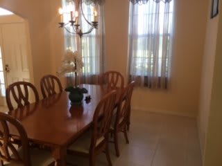 A dining room with a wooden table set, chandelier, and windows with sheer curtains.