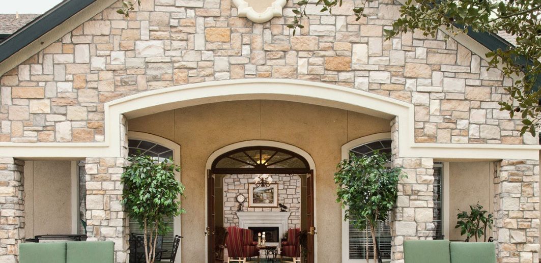 A charming stone facade with an arched entryway leading to a cozy outdoor seating area adorned with potted plants.