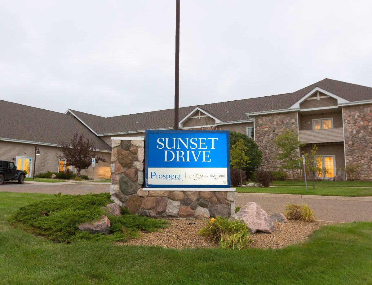 A sign for Sunset Drive Apartments in front of a residential building.