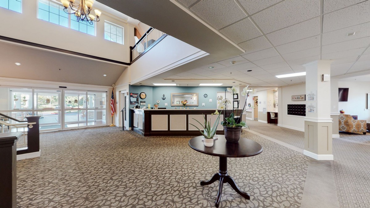 A spacious and well-lit lobby with a reception desk, decorative plants, and patterned carpeting.