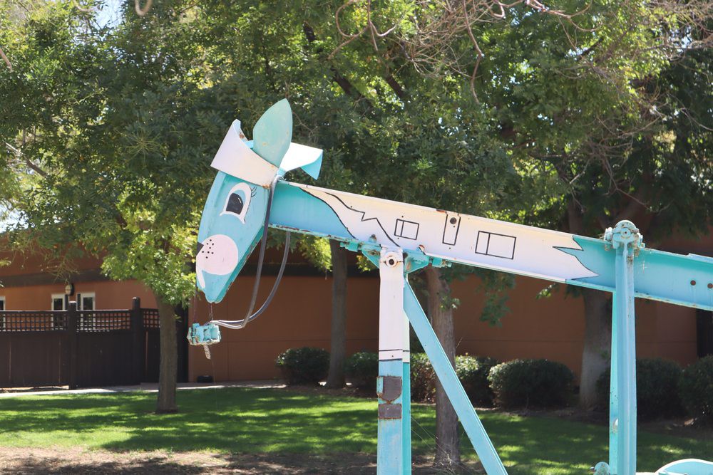 A whimsical blue metal horse sculpture standing outdoors surrounded by trees.