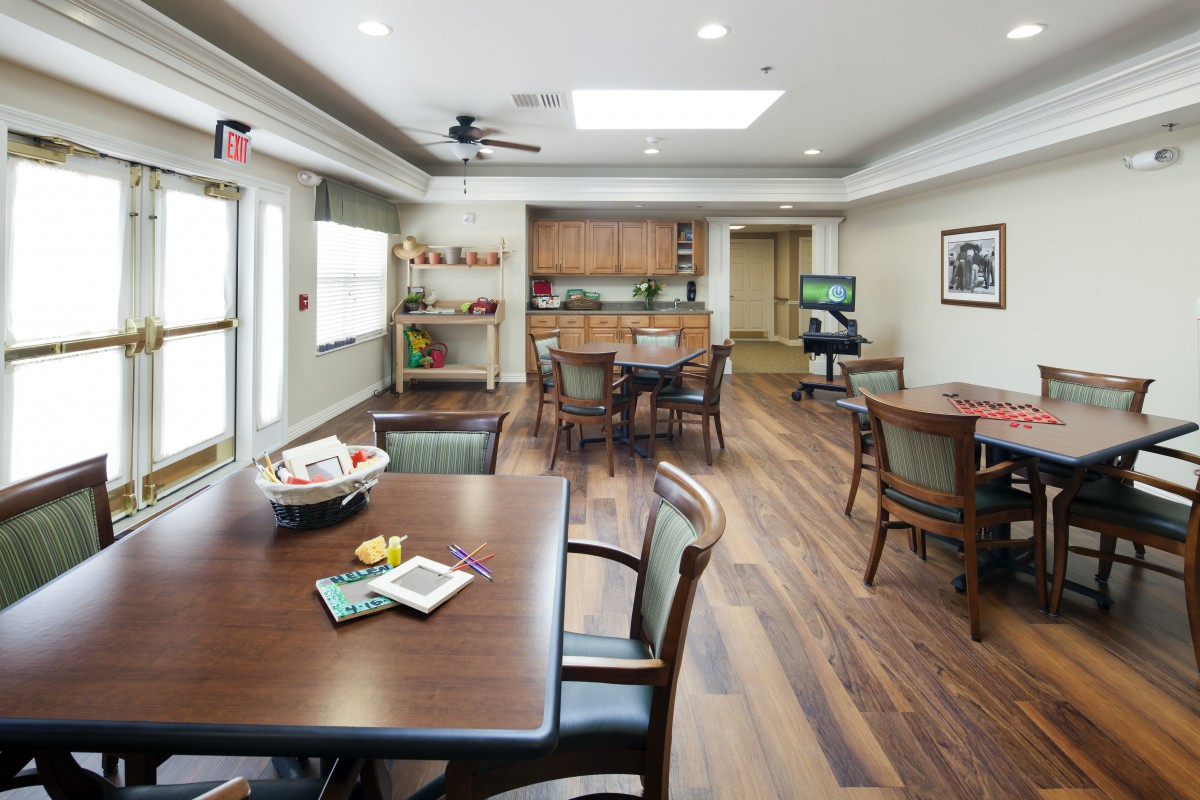 A well-lit dining and kitchenette area with wooden floors and multiple tables and chairs.