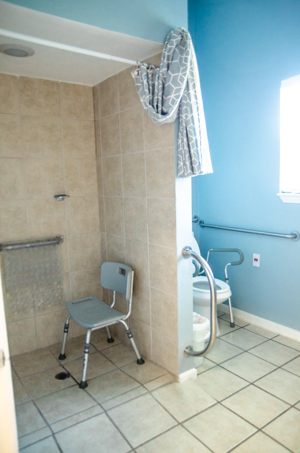 An accessible bathroom with a shower area equipped with grab bars and a shower chair.