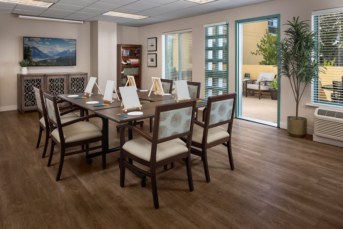 A modern conference room with a wooden table and chairs, featuring ample natural light.