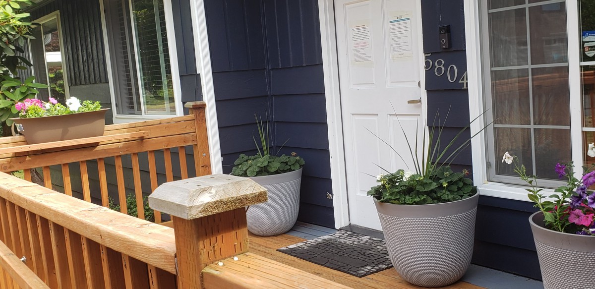 A house entrance with a wooden deck and planters flanking the doorway.