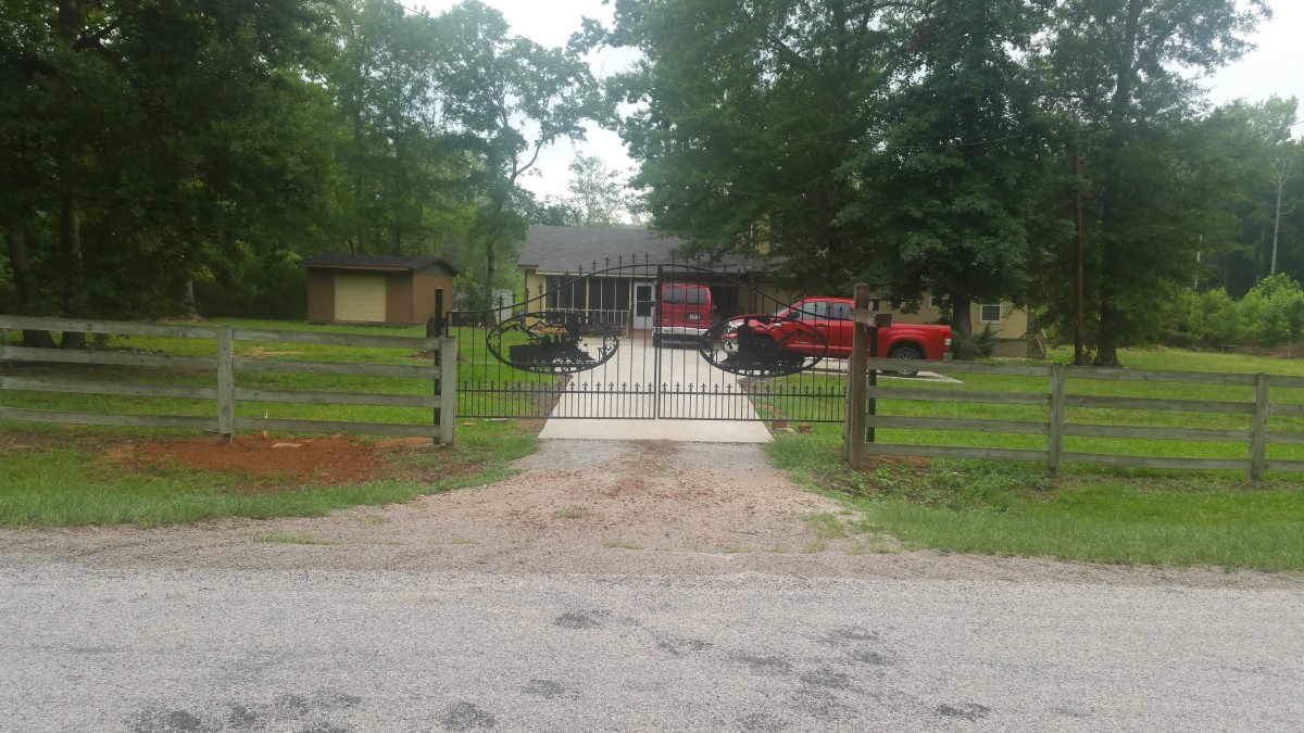 A view of a residential house with a gated driveway and cars parked in front.
