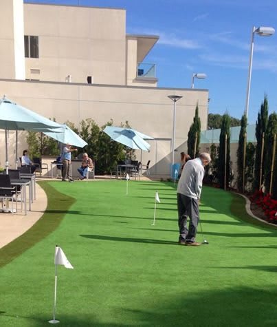 People enjoying a game on the outdoor putting green under clear blue skies.
