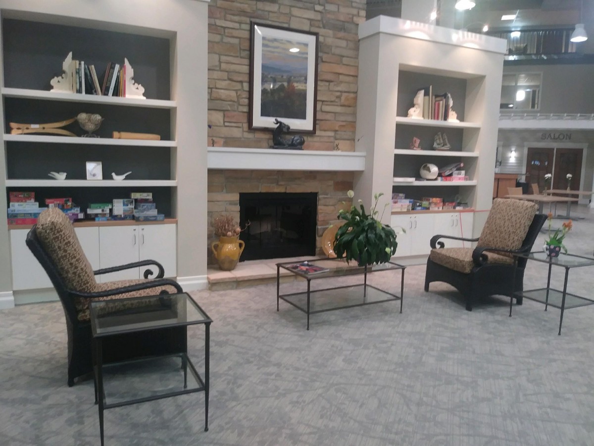 A cozy living room with a central fireplace, surrounded by shelves and comfortable chairs.
