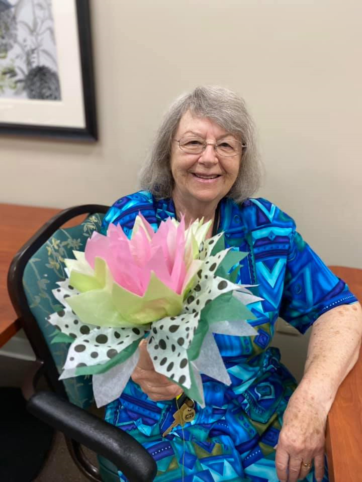 An elderly woman smiling while holding a bouquet of flowers indoors.