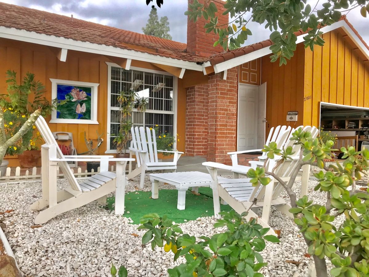 A cozy patio area with white chairs and a brick chimney outside a charming house.