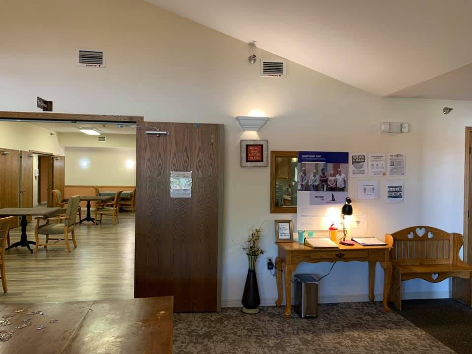 A cozy waiting area featuring a wooden desk with brochures and a lamp, decorated with vases, next to an open doorway leading to a seating area.