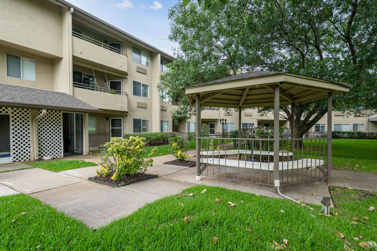 A well-maintained residential apartment complex with a gazebo surrounded by lush greenery.