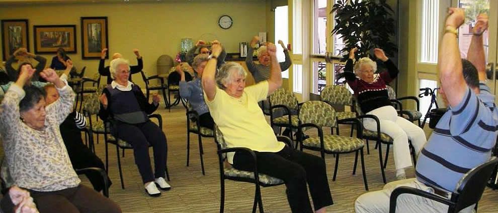 A group of seniors engaging in seated exercises in a community room.