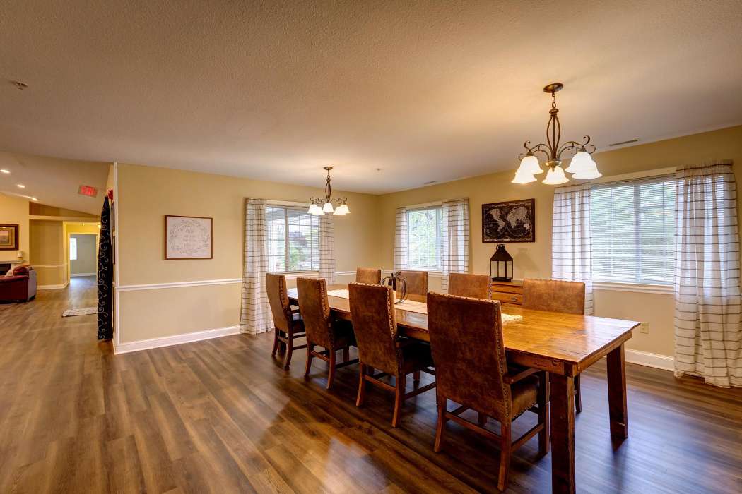 A spacious dining room with a large wooden table and chairs, illuminated by chandeliers.