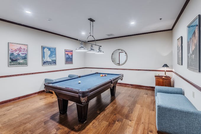 A stylish billiard room featuring a pool table, wooden floors, modern lighting, and decorative wall art.