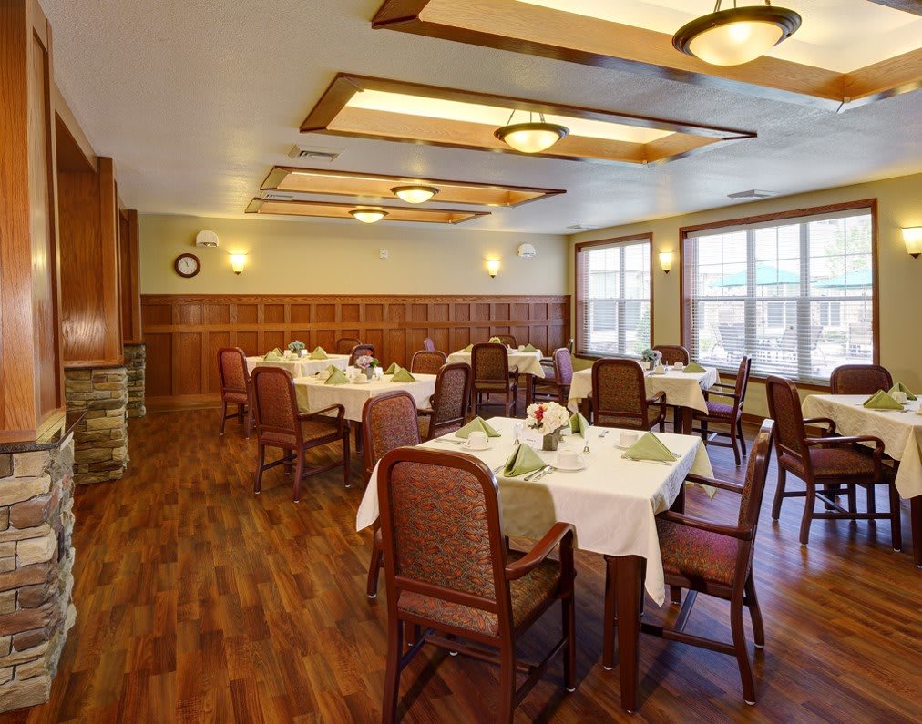 A cozy dining room with several tables and chairs, featuring elegant lighting and wooden floors.