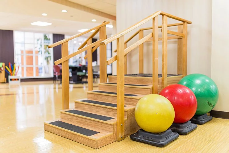 Physical therapy setup with wooden stairs and balance balls for rehabilitation exercises.
