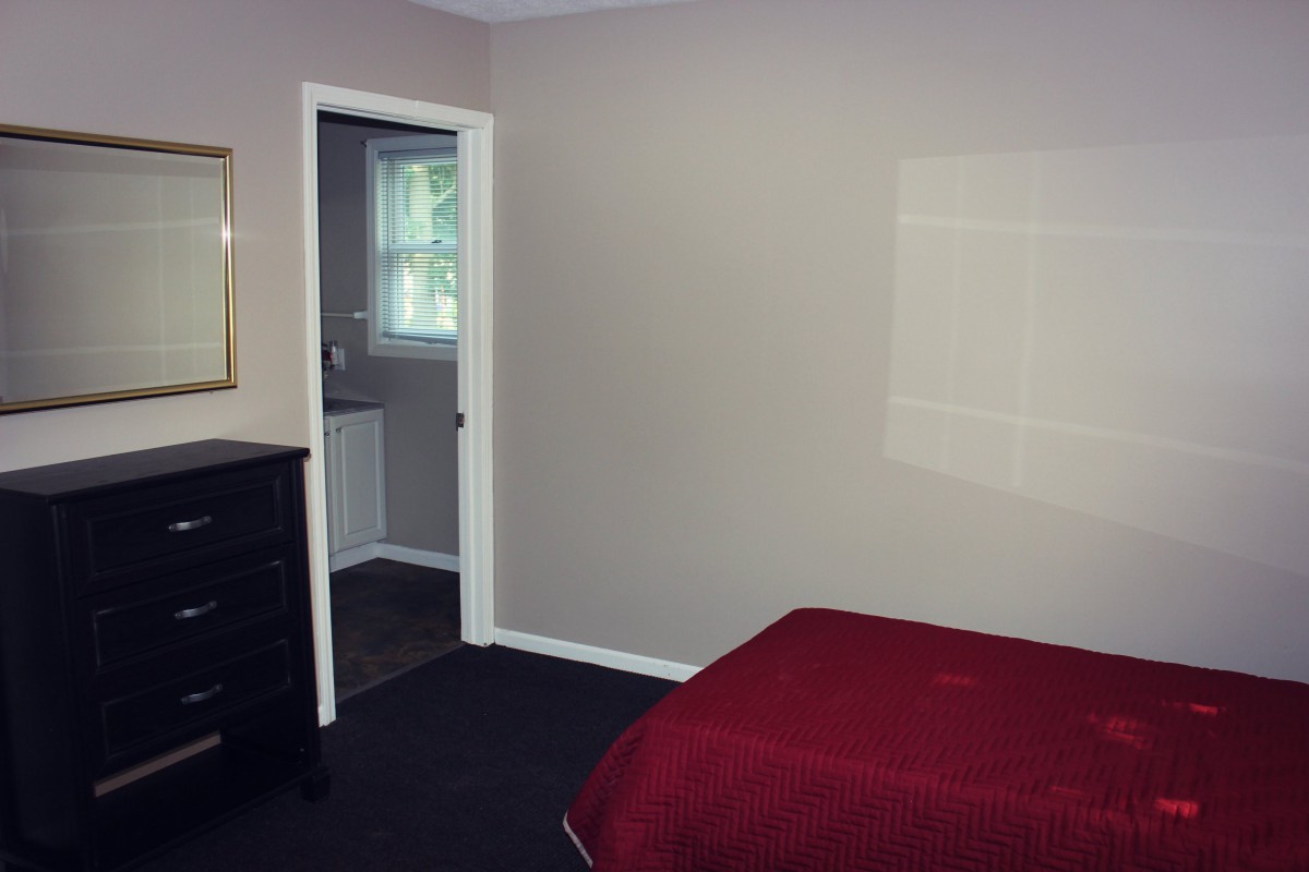 A simple bedroom with a red bedspread, dresser, and an open doorway leading to a bathroom.