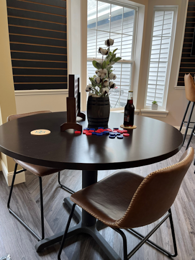 A cozy dining setup featuring a round black table adorned with decorative flowers and game pieces, complemented by stylish chairs.